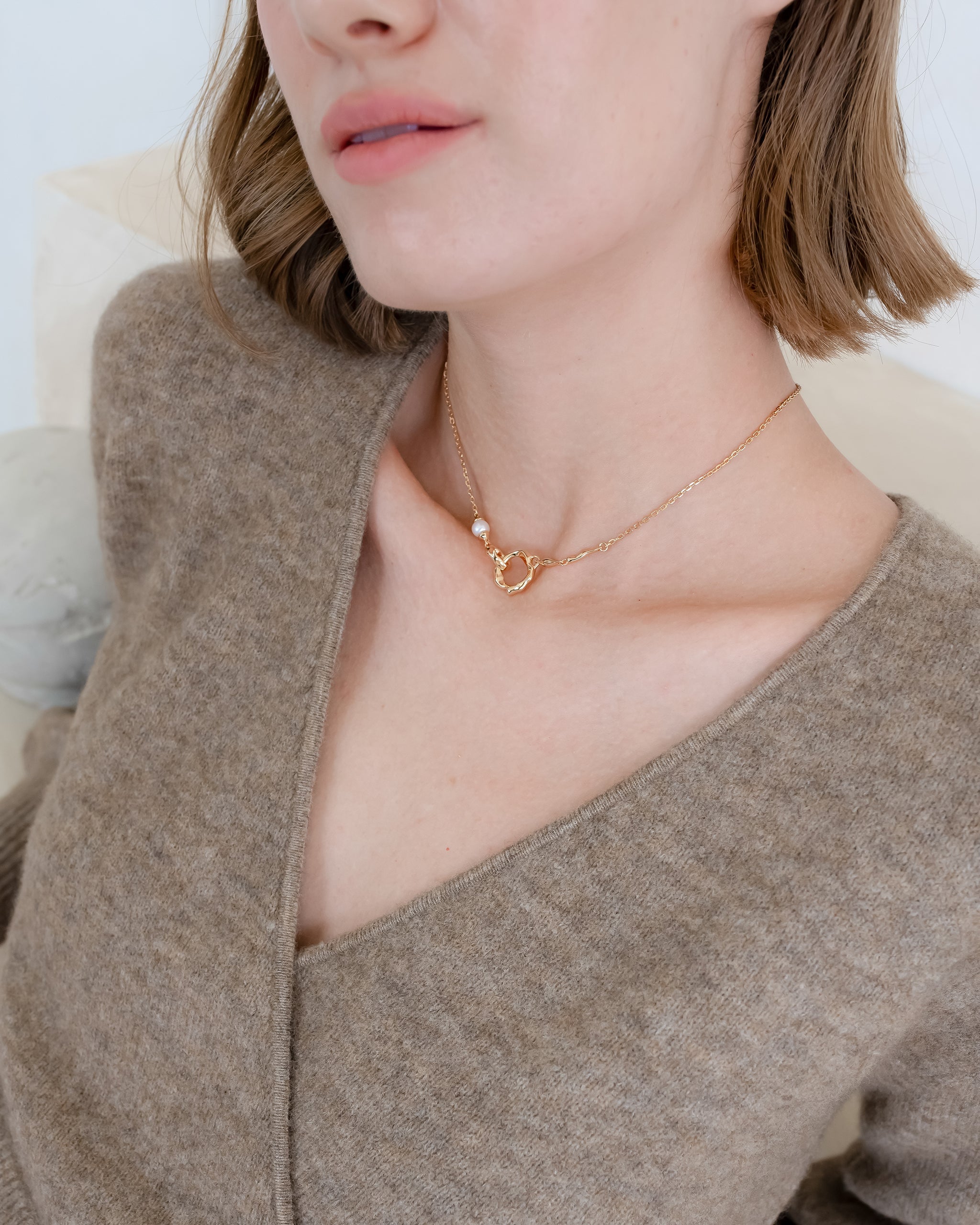 Person wearing a brown sweater and gold necklace with a minimal background